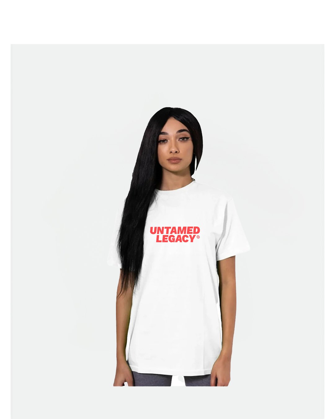 "Female model with long black hair wearing a white Untamed Legacy t-shirt in a minimalist studio setting, showcasing bold streetwear branding